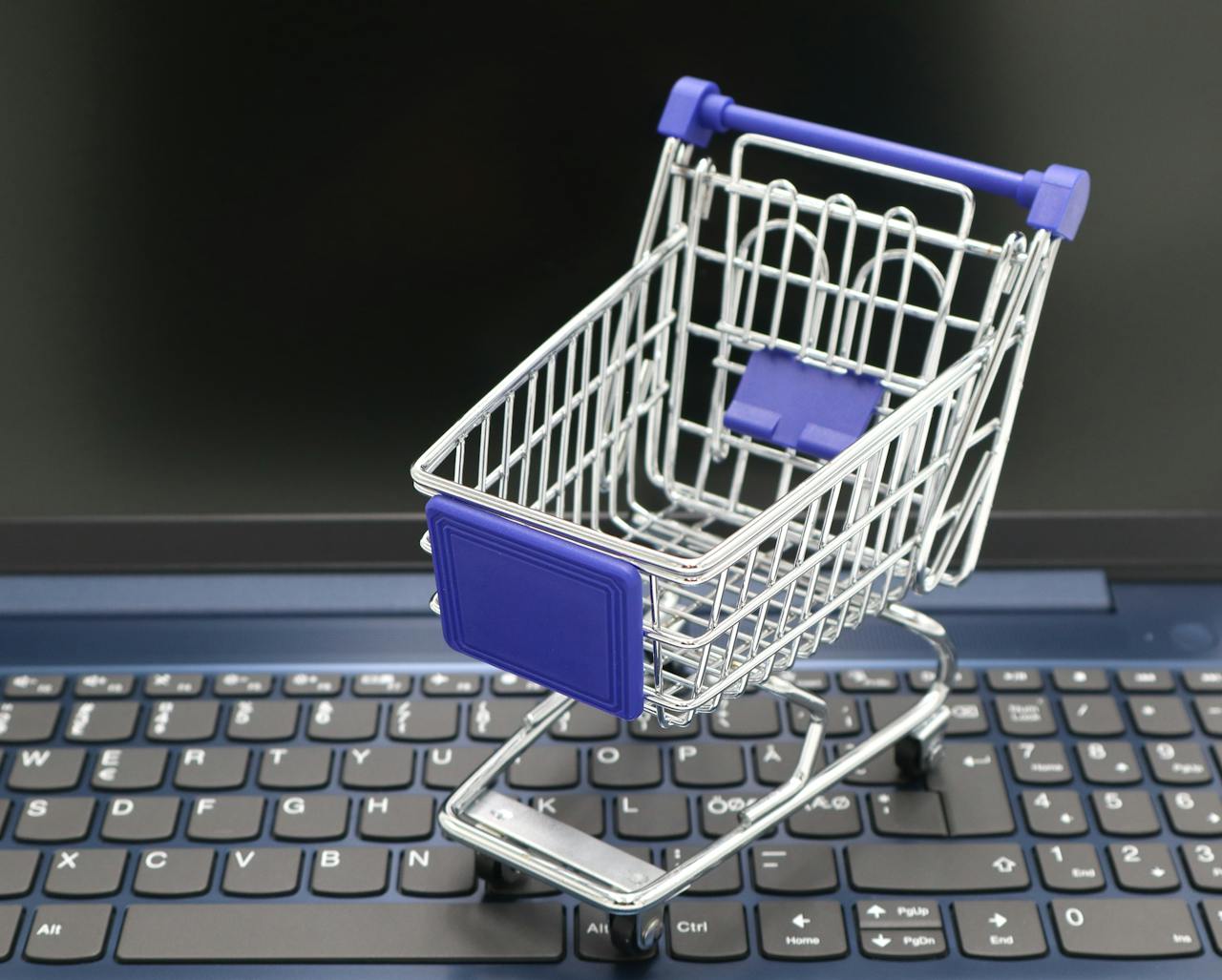 A mini shopping cart placed on a laptop keyboard, symbolizing online shopping and digital retail.